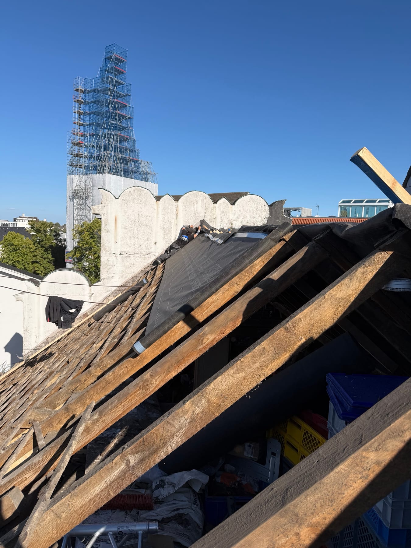 Die neue Unterspannbahn wird über den First des Capitol-Dachs gezogen, im Hintergrund der eingerüstete Kirchturm